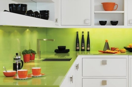 Het aanrechtblad en schort van een heldere limoen tint zien er geweldig uit in combinatie met witte keukenfronten en oranje schalen.